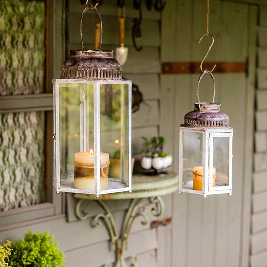 Two hanging lanterns with candles inside on a porch.