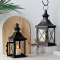 Two black lanterns with candles on a surface with a decorative mirror and plant in the background.