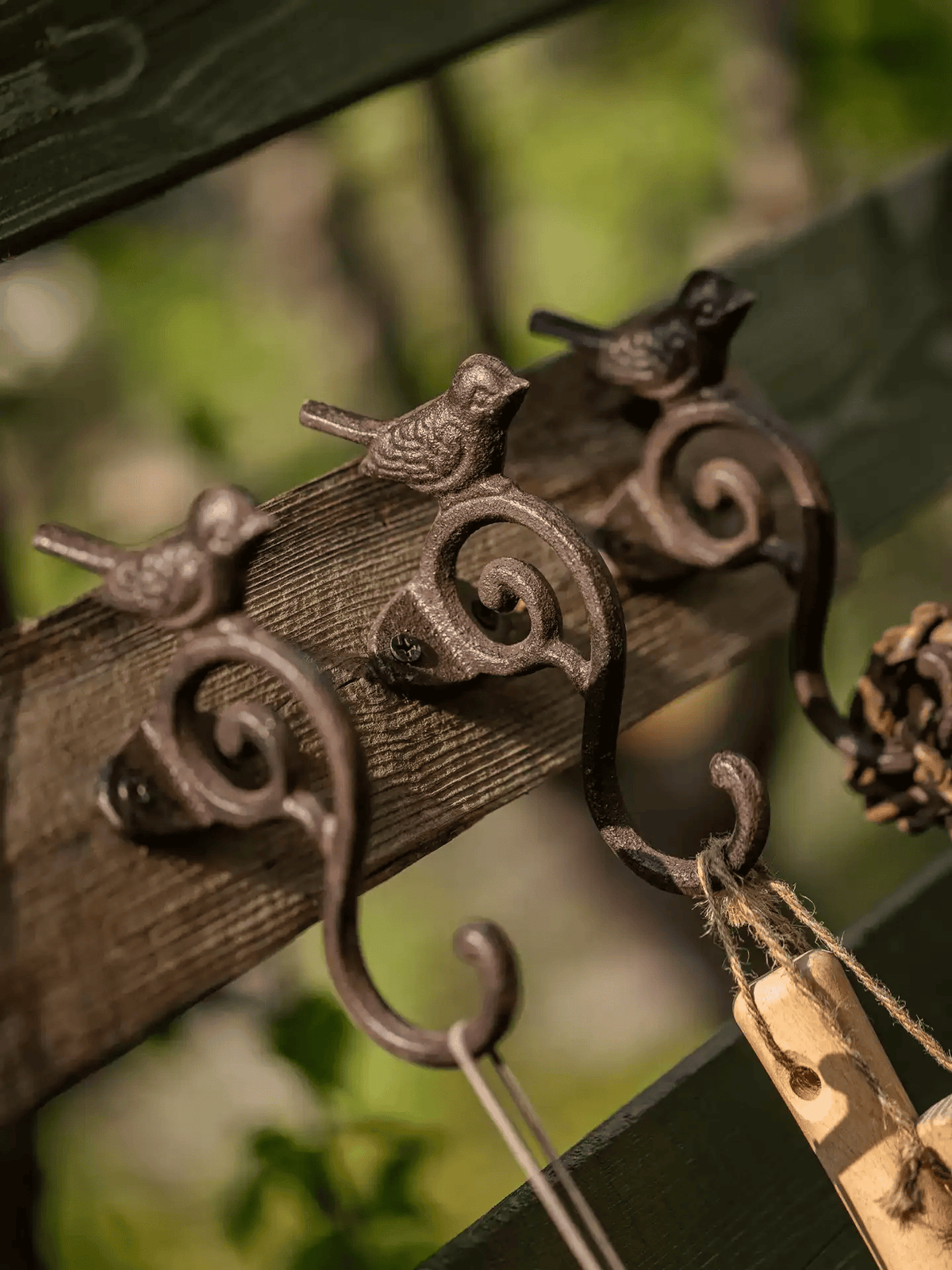 Decorative metal hook with bird designs on a wooden surface, blurred green background