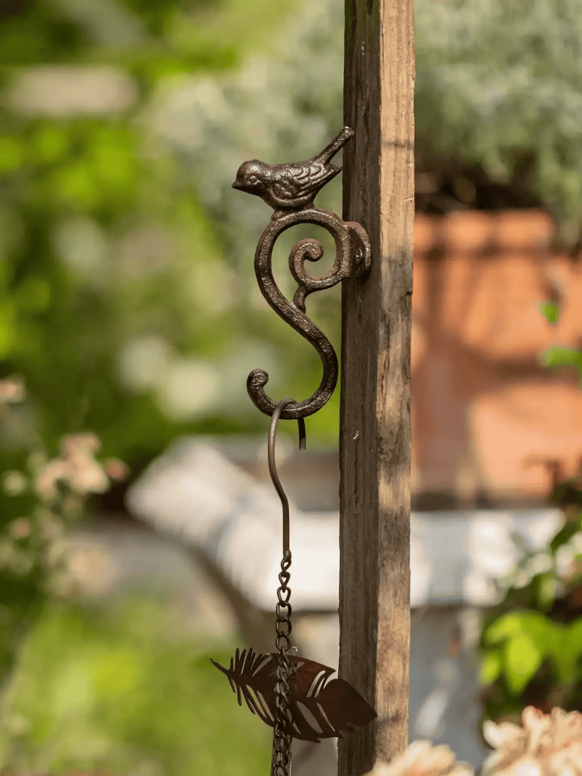 Decorative metal hook with bird design on a wooden post against a blurred garden background