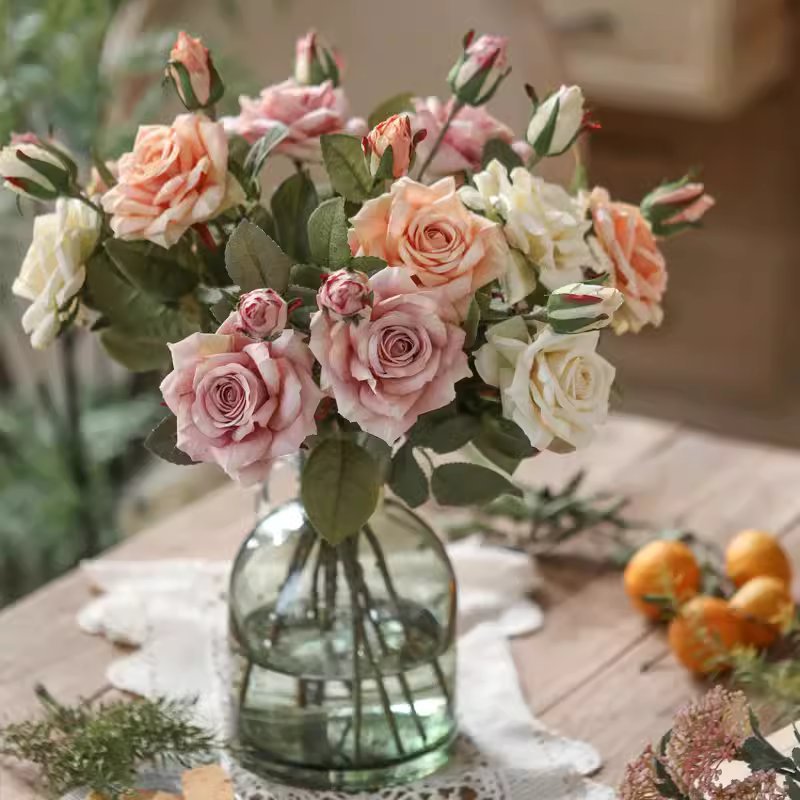 Bouquet of pink and white roses in a clear glass vase on a wooden table.