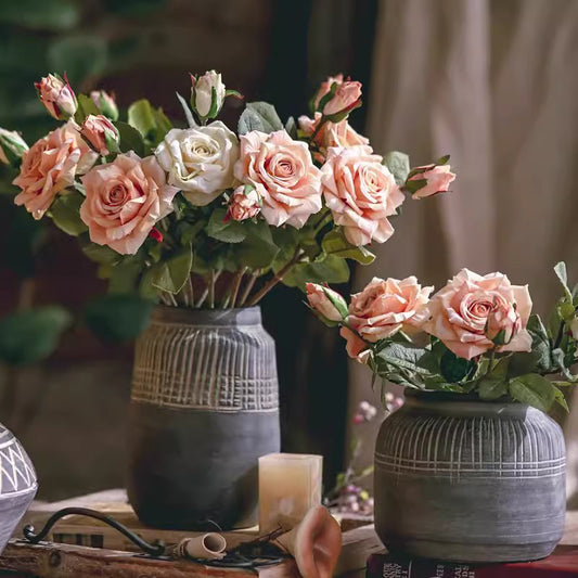 Two gray textured vases with pink and white roses on a wooden surface.