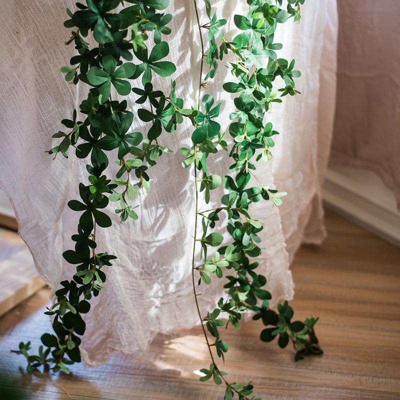 Artificial green leaves hanging in front of a white curtain