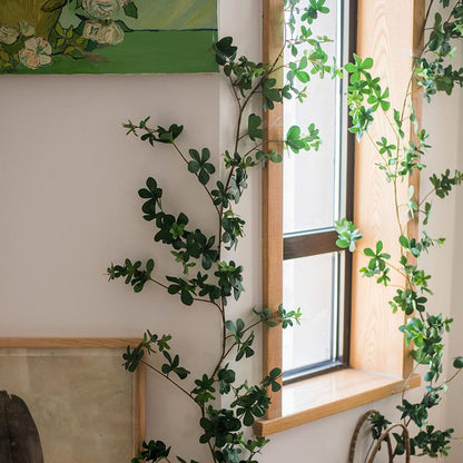 Green leafy branches in front of a window with a painting on the wall.