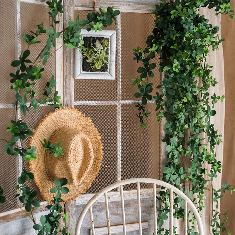 Wicker chair with a straw hat and greenery against a wooden paneled wall.