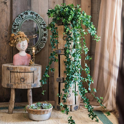 Decorative setting with a wooden barrel, plant, and small statue against a rustic wall.